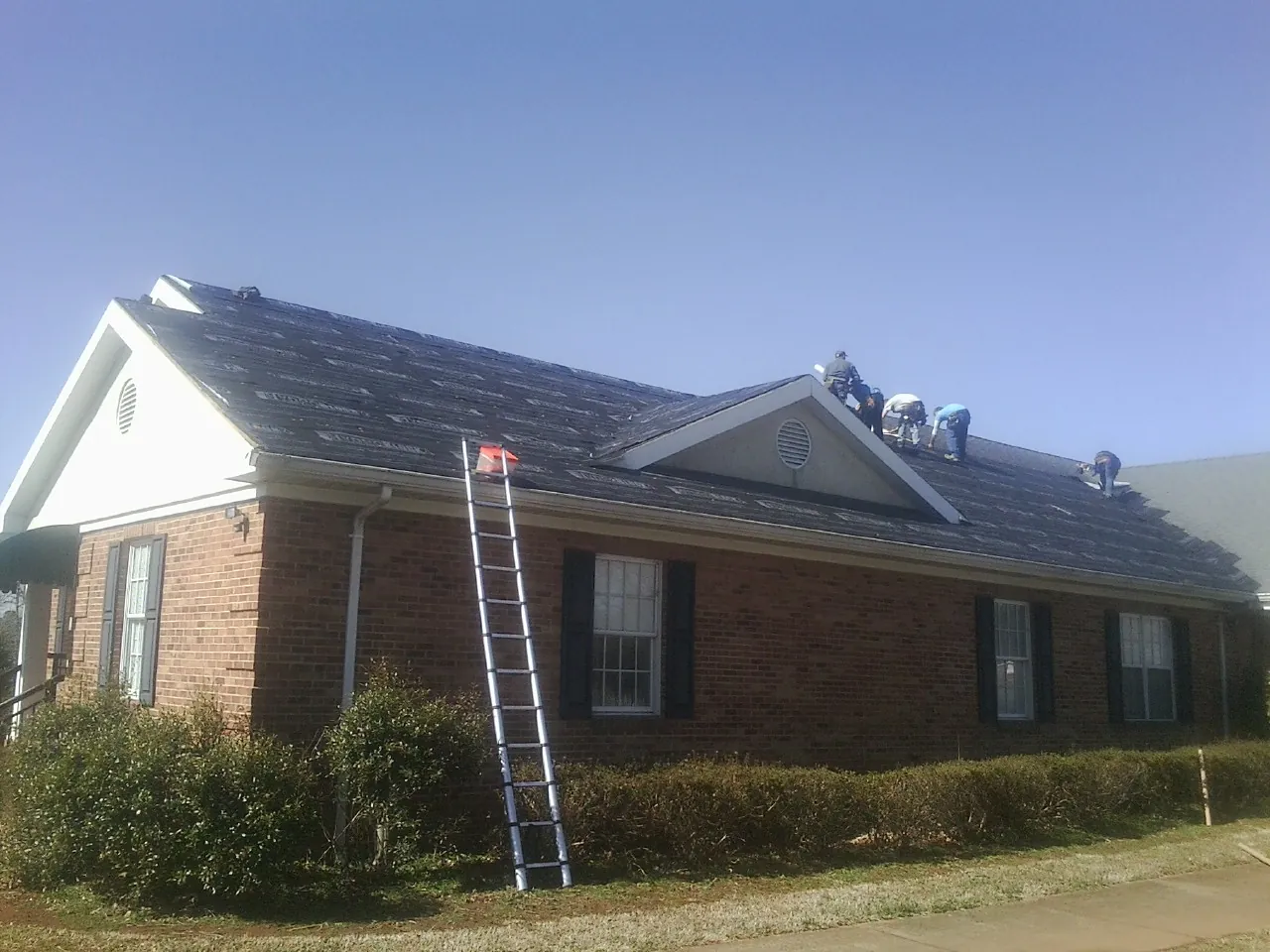 Crew tearing shingles off a brick ranch roof with a ladder set — Metal Roof Repair work by our crew in Galesburg