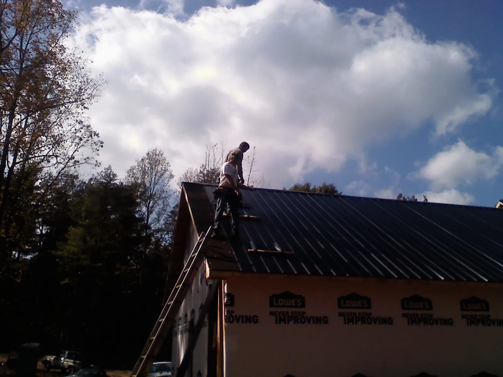 Roofer fastening dark metal panels high against a cloudy sky, from a Roof Inspection job in Galesburg
